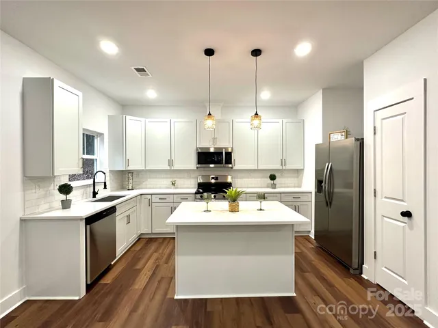 a large white kitchen with kitchen island a sink stainless steel appliances and cabinets