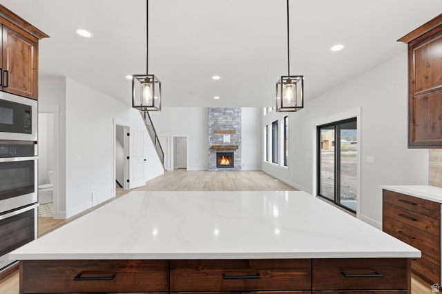 2970 North Mahogany Vly Road Logan, UT 84341 - Photo 39 of 39 Kitchen with dark wood finish cabinetry, a stone fireplace, light stone countertops, open floor plan, and stainless steel appliances