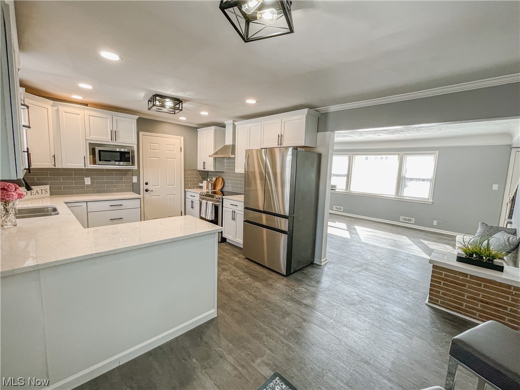 24709 Emery Road Warrensville Heights, OH 44128 - Photo 11 of 34 Kitchen with white cabinets, tasteful backsplash, dark hardwood / wood-style floors, appliances with stainless steel finishes, and wall chimney exhaust hood