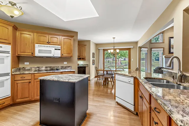 a kitchen with stainless steel appliances granite countertop a stove top oven a sink dishwasher a dining table and chairs with wooden floor