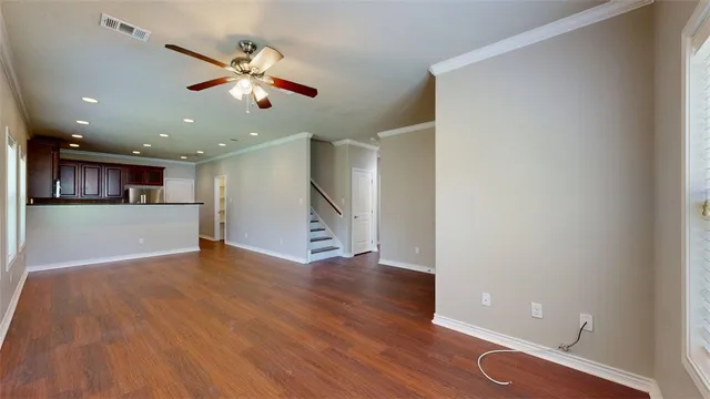 a view of an empty room with wooden floor and a ceiling fan