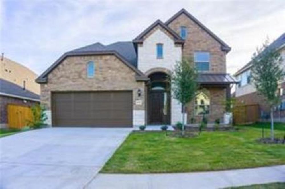 Two-story residence featuring a brick and stone facade, arched entryway, and a two-car garage with a concrete driveway