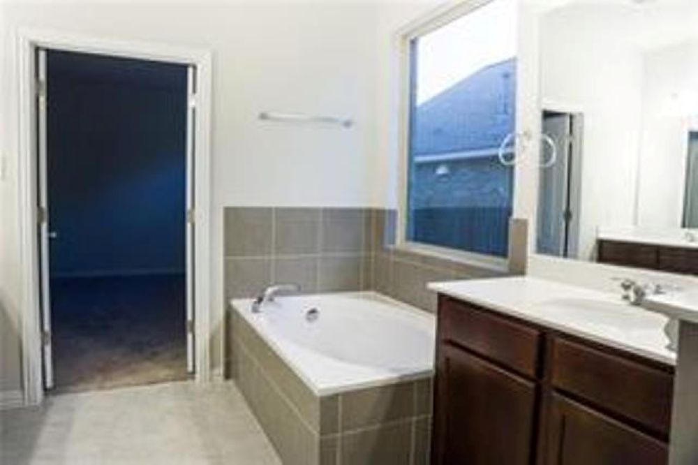 4021 Gildas Path Pflugerville, TX 78660 - Photo 11 of 19 Bathroom featuring a built-in tub with tile surround, a dual vanity with undermount sinks, a large mirror, and a window