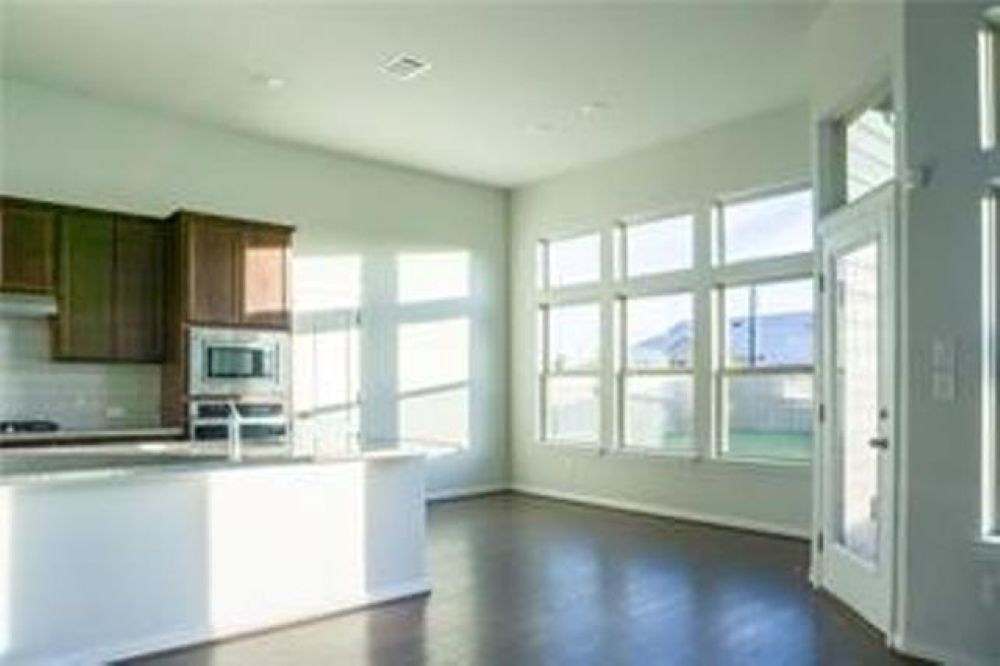 4021 Gildas Path Pflugerville, TX 78660 - Photo 4 of 19 Open-concept living area featuring dark wood-finish flooring, a contemporary kitchen island with a white countertop, and a wall of multi-pane windows providing abundant natural light