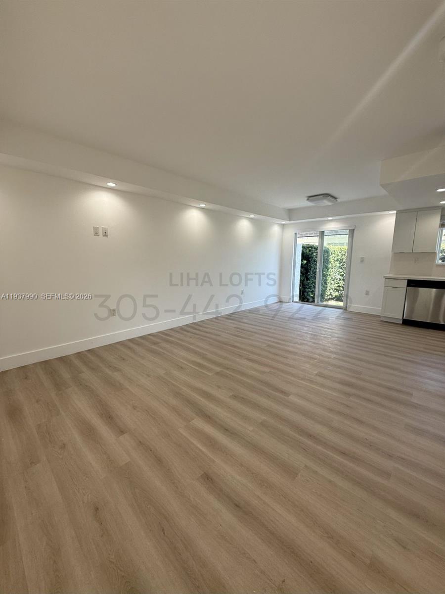 a view of an empty room with wooden floor and a kitchen