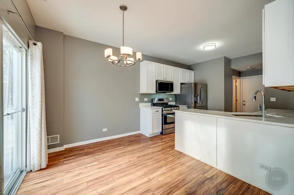 a kitchen with stainless steel appliances granite countertop a refrigerator a stove oven a sink dishwasher and white cabinets with wooden floor