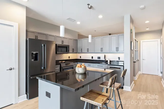 a kitchen with stainless steel appliances granite countertop a dining table chairs refrigerator and microwave