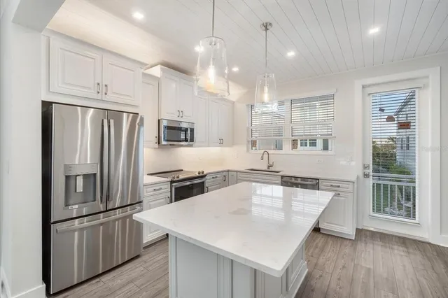 a kitchen with stainless steel appliances granite countertop a refrigerator a sink dishwasher a stove and white countertops with wooden floor