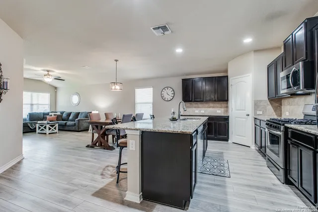a open kitchen with stainless steel appliances granite countertop a stove top oven a sink dishwasher a dining table and chairs with wooden floors