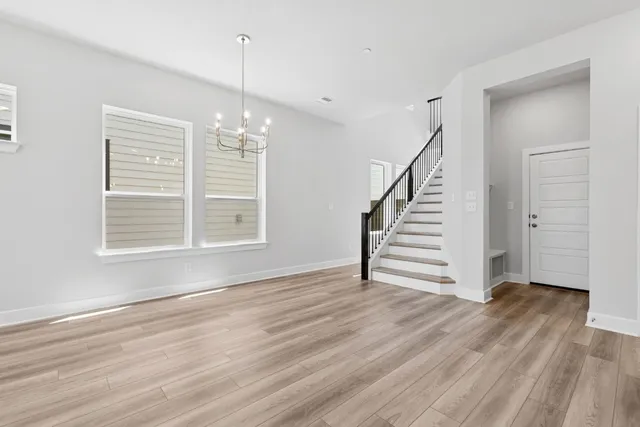 a view of an empty room with wooden floor stairs and a window