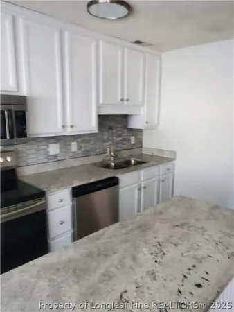 a kitchen with stainless steel appliances granite countertop a stove a sink and white cabinets