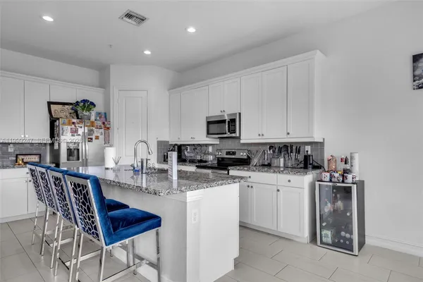 a kitchen with stainless steel appliances granite countertop a stove top oven a sink a refrigerator with white cabinets and wooden floor