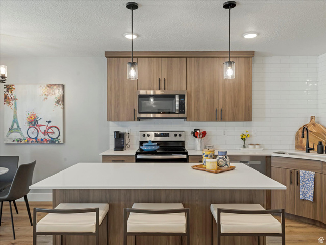 3047 Old Emigrant Road, Unit C Syracuse, UT 84075 - Photo 6 of 20 Kitchen with a kitchen breakfast bar, light wood finished floors, stainless steel appliances, a kitchen island, and a textured ceiling