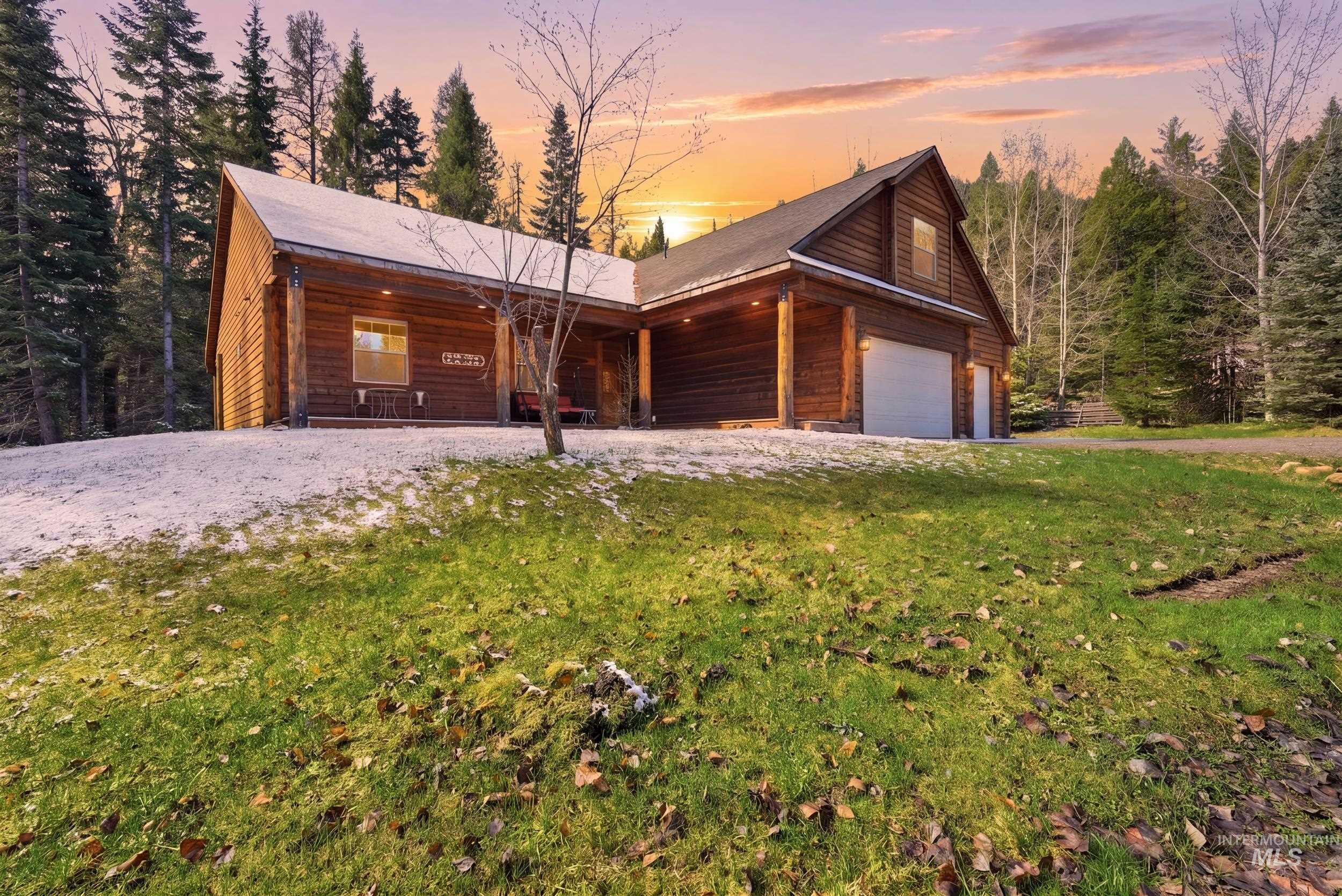 2538 West Mountain Road Donnelly, ID 83615 - Photo 2 of 50 Log-sided residence featuring an attached garage with a white door, a covered porch with wooden columns, and an upper-level dormer