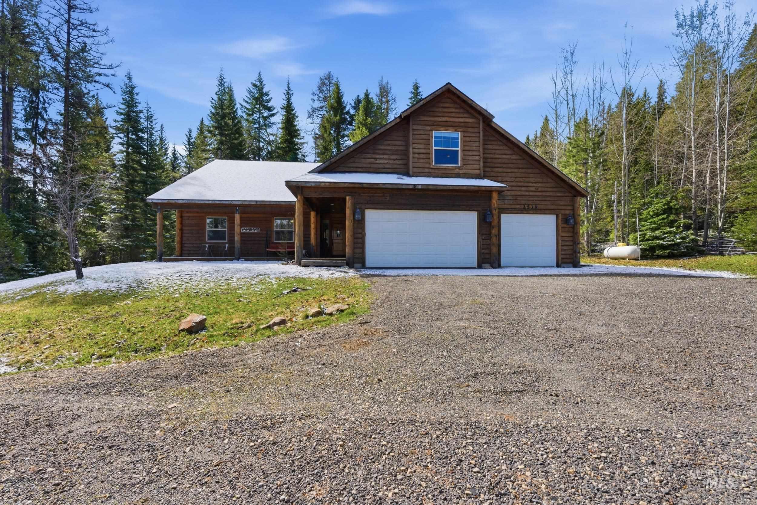 2538 West Mountain Road Donnelly, ID 83615 - Photo 34 of 50 Rustic wood-sided home featuring a covered front porch, two-car garage, and surrounding mature trees