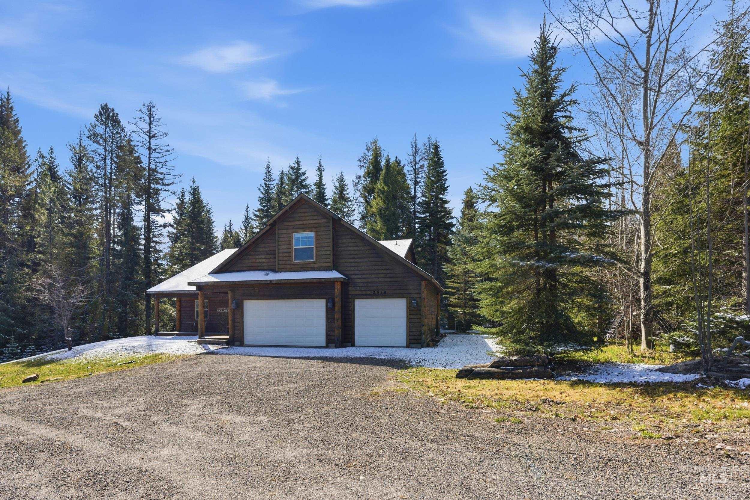 2538 West Mountain Road Donnelly, ID 83615 - Photo 35 of 50 Wood-sided residence featuring a two-car garage with white doors, a gabled roofline, and a covered porch entrance