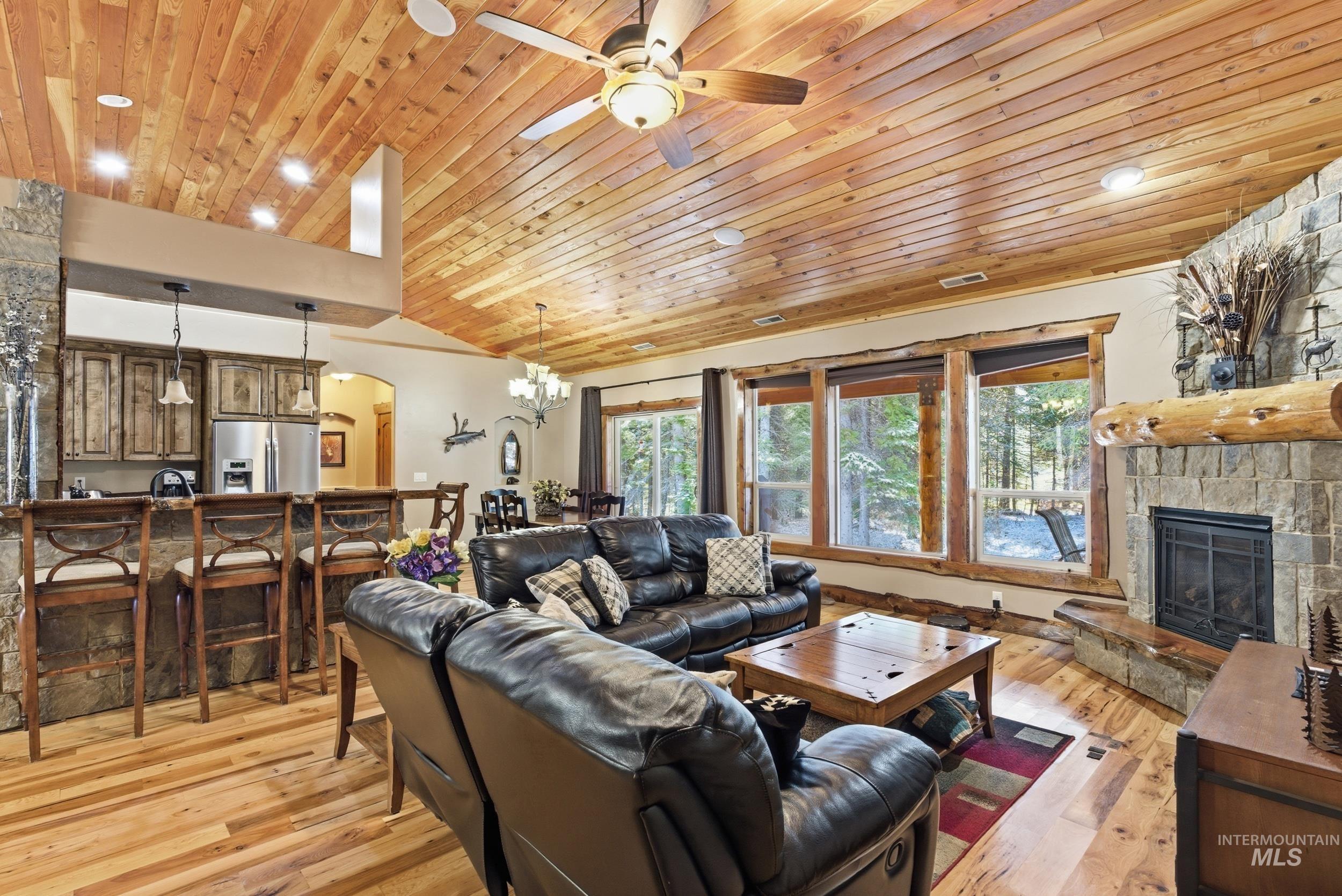 2538 West Mountain Road Donnelly, ID 83615 - Photo 7 of 50 Spacious living area featuring a vaulted wood-finish ceiling with a ceiling fan, a stone-clad fireplace with a log mantel, and expansive windows