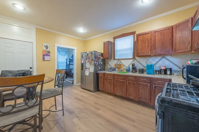 a kitchen with stainless steel appliances granite countertop a refrigerator a sink a stove and chairs with wooden floor