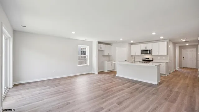 a large white kitchen with kitchen island a sink wooden floor and a refrigerator