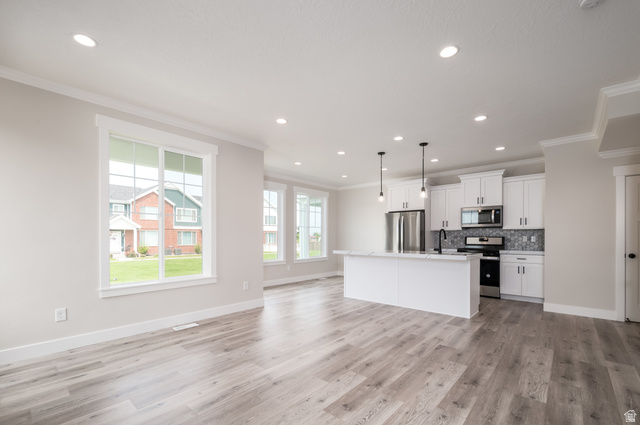 8797 Green Way, Unit 3 Sandy, UT 84094 - Photo 11 of 12 Kitchen featuring decorative light fixtures, a center island with sink, white cabinets, crown molding, and open floor plan