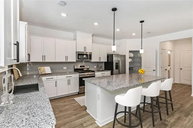 a kitchen with stainless steel appliances kitchen island granite countertop a sink a microwave a refrigerator and white cabinets