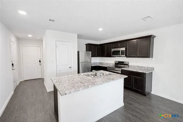 a kitchen with stainless steel appliances granite countertop a stove top oven a refrigerator a sink and dishwasher with wooden floor