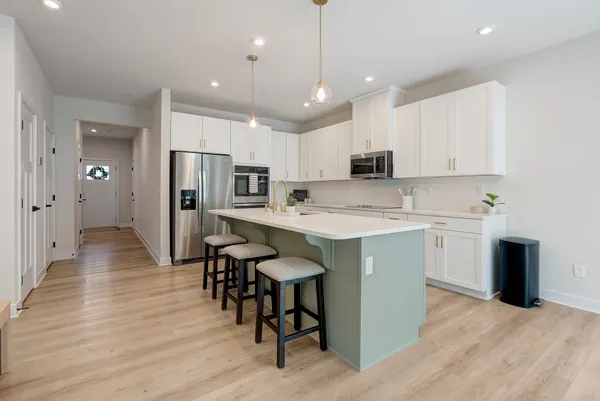 a kitchen with stainless steel appliances granite countertop a refrigerator a sink dishwasher a stove and white cabinets with wooden floor