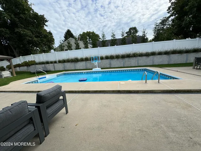 a view of swimming pool with seating space and trees in the background