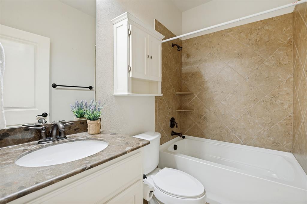 4646 G Rhett Lane Carrollton, TX 75010 - Photo 12 of 16 Bathroom featuring a single vanity with a patterned countertop and undermount sink, a white built-in storage cabinet, and a bathtub with full tile surround and oil-rubbed bronze fixtures