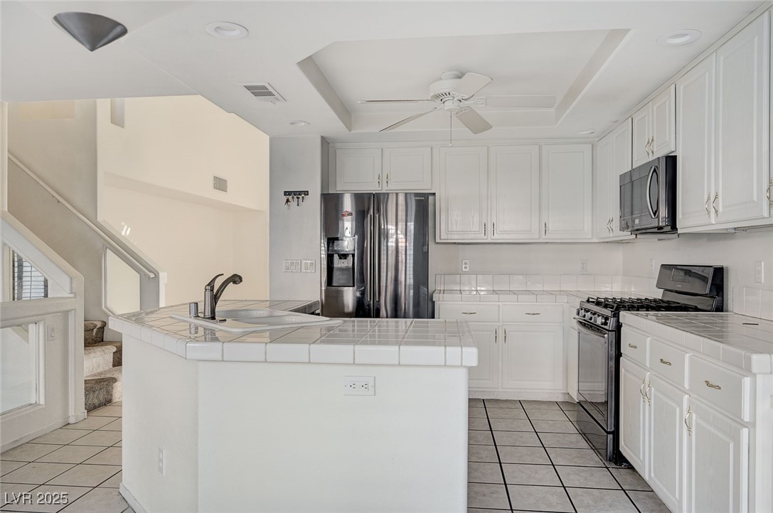 8776 Country View Avenue Las Vegas, NV 89129 - Photo 11 of 43 Kitchen featuring tile countertops, stainless steel appliances, a tray ceiling, light tile patterned flooring, and white cabinetry