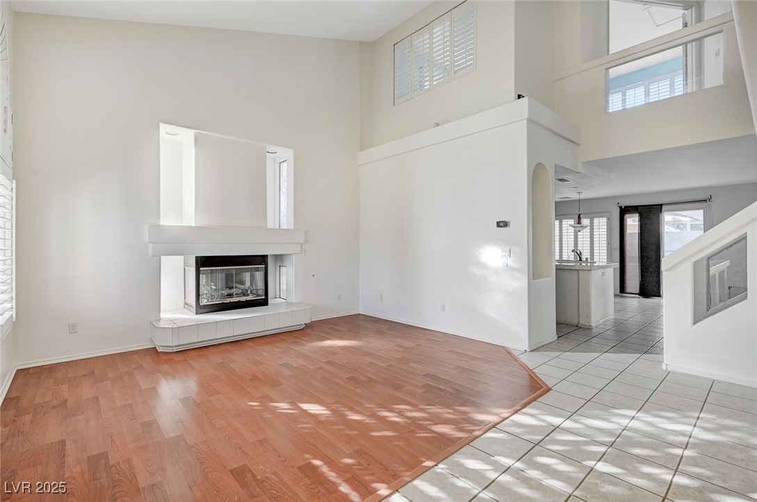 8776 Country View Avenue Las Vegas, NV 89129 - Photo 4 of 43 Unfurnished living room featuring light wood-style floors, a high ceiling, a tile fireplace, and arched walkways