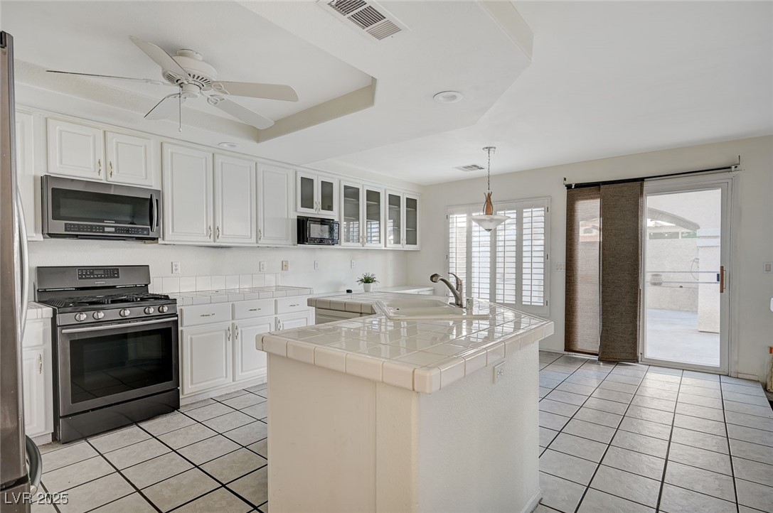 8776 Country View Avenue Las Vegas, NV 89129 - Photo 8 of 43 Kitchen featuring stainless steel appliances, light tile patterned floors, white cabinets, glass insert cabinets, and decorative light fixtures
