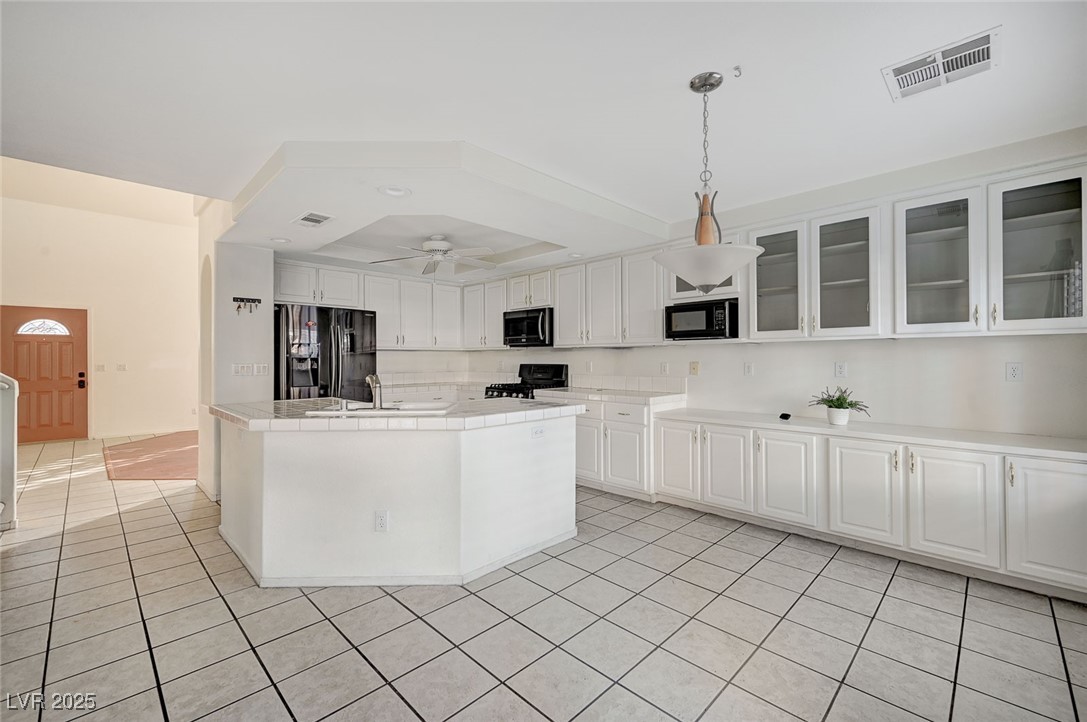 8776 Country View Avenue Las Vegas, NV 89129 - Photo 9 of 43 Kitchen featuring white cabinets, a kitchen island with sink, black appliances, light tile patterned flooring, and pendant lighting