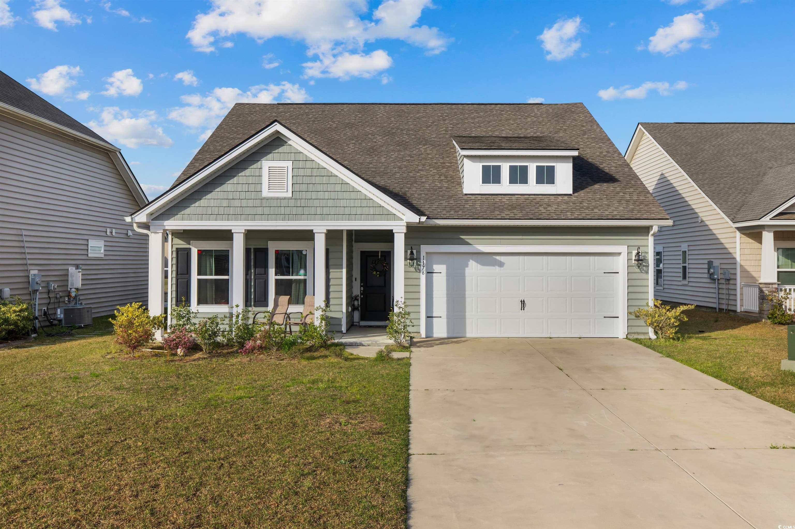 View of front of property with central air condition unit, an attached garage, a front lawn, roof with shingles, and covered porch