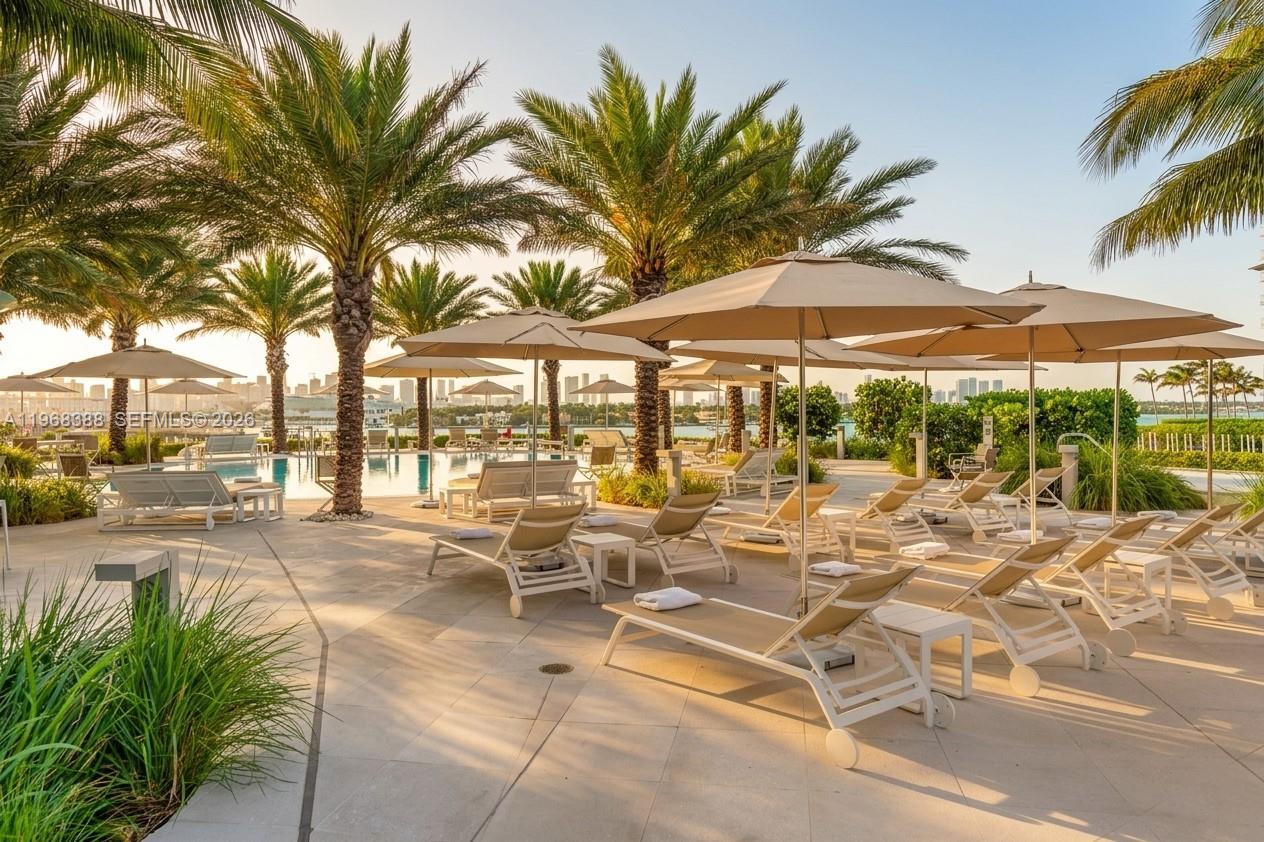 450 Alton Road, Unit 1202 Miami Beach, FL 33139 - Photo 35 of 68 a view of a patio with a dining table and chairs under an umbrella with palm trees