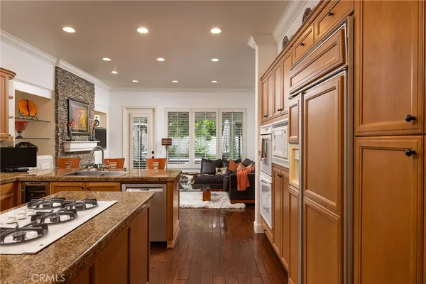 a kitchen with stainless steel appliances granite countertop a refrigerator a sink dishwasher a stove and a dining table with wooden floor