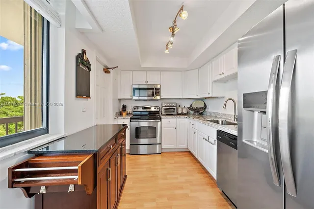 a kitchen with stainless steel appliances granite countertop a refrigerator a stove oven a sink dishwasher and white cabinets with wooden floor