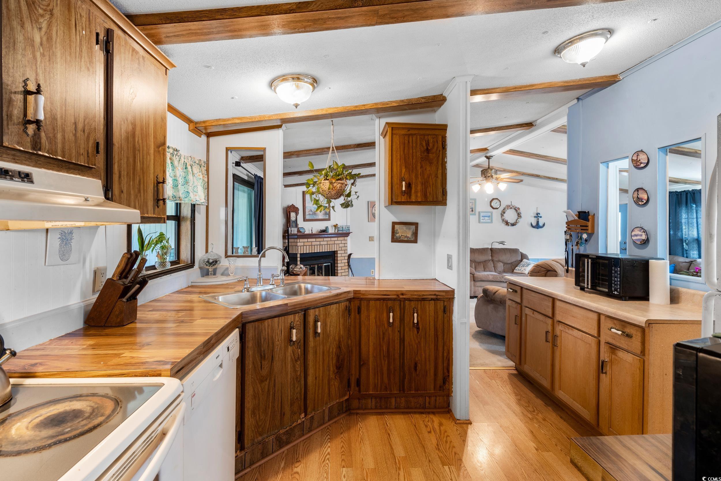 17 Crooked Island Circle Murrells Inlet, SC 29576 - Photo 12 of 39 Kitchen with white dishwasher, a sink, light wood-style floors, a brick fireplace, and under cabinet range hood