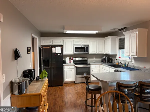 a kitchen with stainless steel appliances granite countertop a stove top oven a refrigerator a sink a dining table and chairs with wooden floor