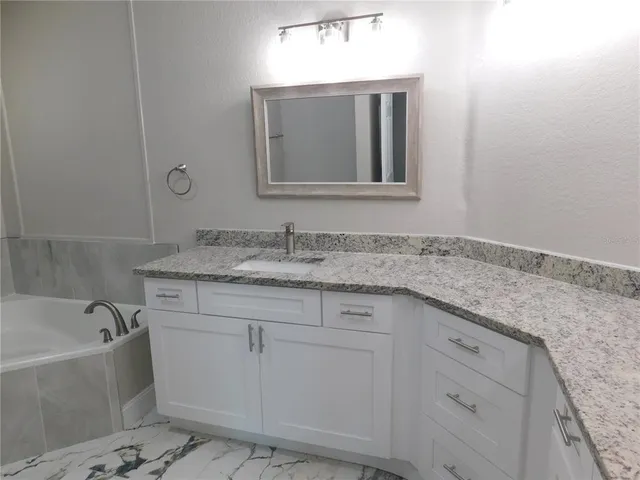 a bathroom with a granite countertop bathtub sink vanity and mirror