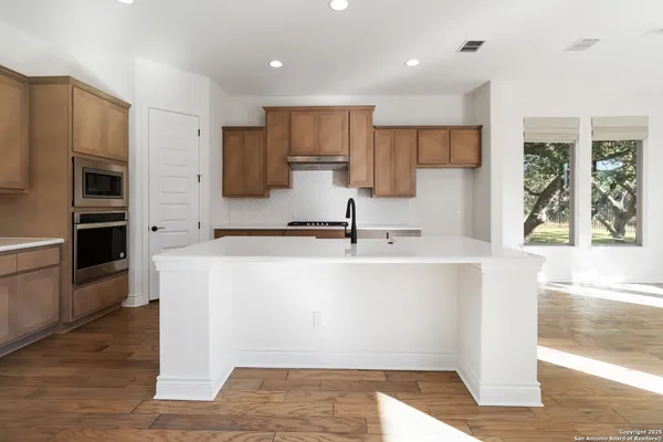 a view of kitchen with stainless steel appliances granite countertop a stove a sink a refrigerator and white cabinets with wooden floor