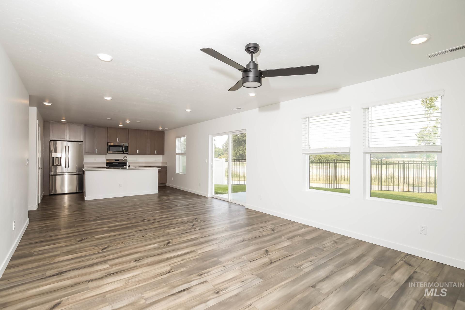 Spacious open-concept living area with wood-finish flooring, recessed lighting, and a modern ceiling fan