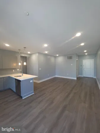 a large hall with a refrigerator a sink dishwasher with a dining table chairs and wooden floor