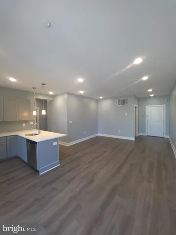 a large hall with a refrigerator a sink dishwasher with a dining table chairs and wooden floor