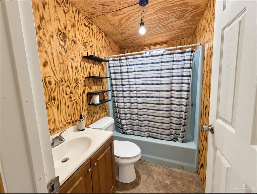 0 Fm 1015 Edcouch, TX 78538 - Photo 9 of 20 Wood paneling on walls and ceiling, single vanity with integrated sink, white toilet, wall-mounted shelving, and a built-in shower/tub combination