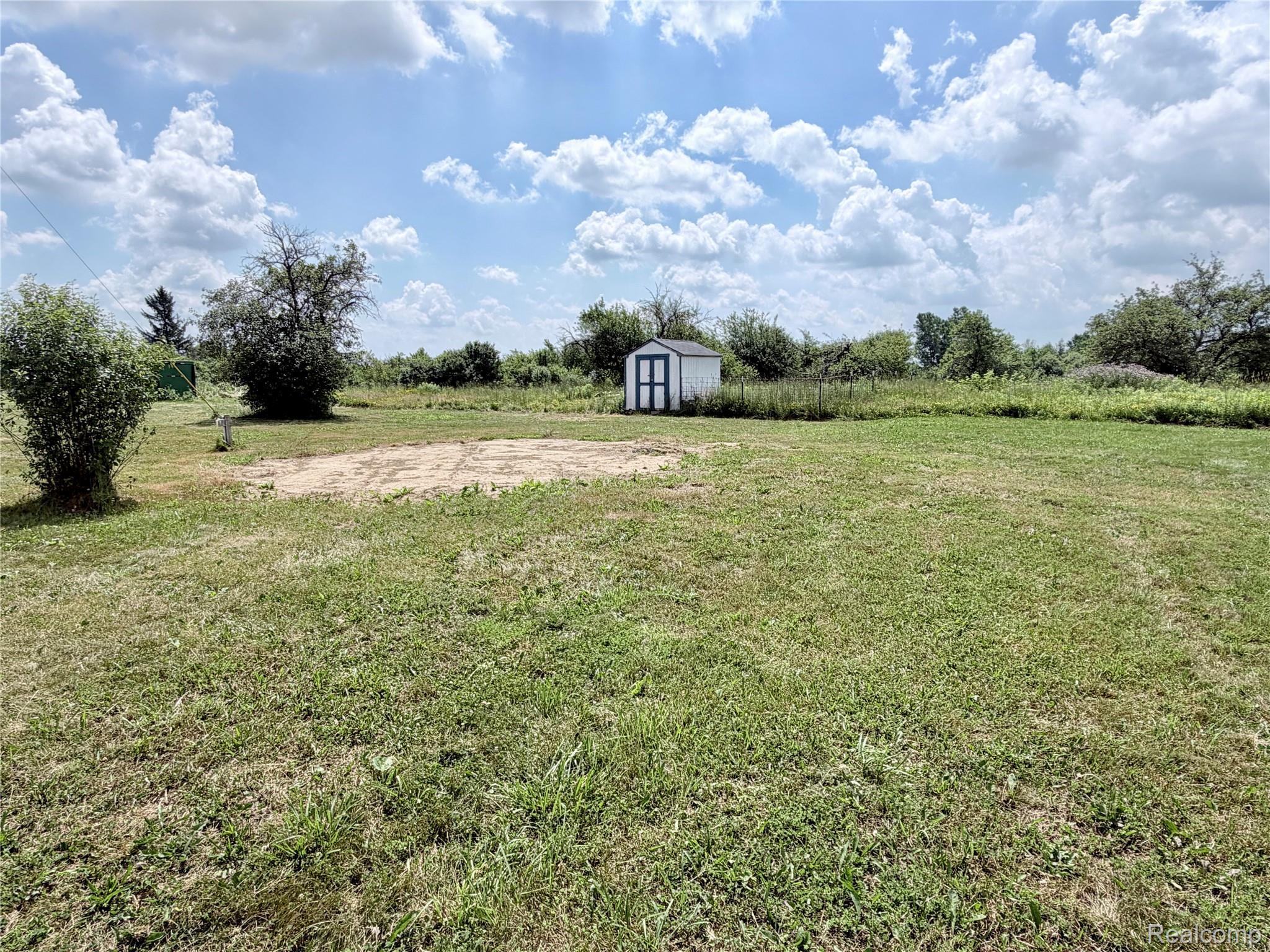 10865 Norman Road Yale, MI 48097 - Photo 20 of 23 Spacious lawn with a white storage shed featuring dark trim doors, a clear sky overhead, and mature trees bordering the property