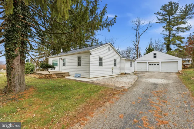 a view of a white house next to a yard with a large tree