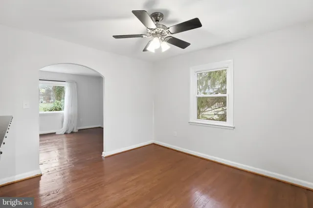 an empty room with wooden floor chandelier fan and windows