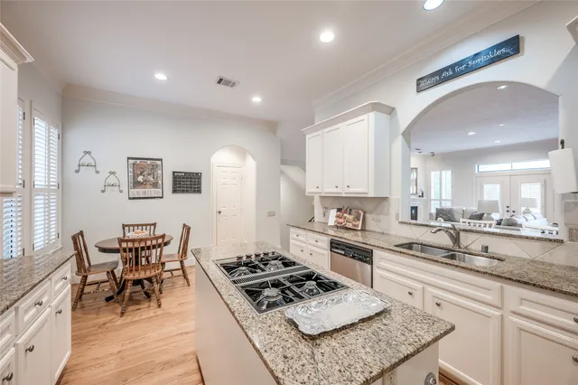 a kitchen with stainless steel appliances granite countertop a stove top oven a sink a dining table and chairs with wooden floor