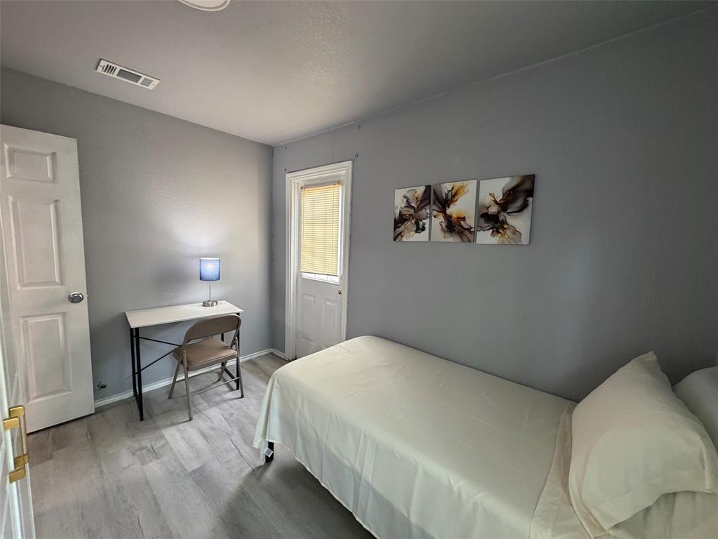 714 Southwest Dallas Street Grand Prairie, TX 75051 - Photo 11 of 27 Room featuring light gray walls, wood-finish flooring, a white interior door with gold-tone hardware, and a white exterior door with a window and bamboo blinds
